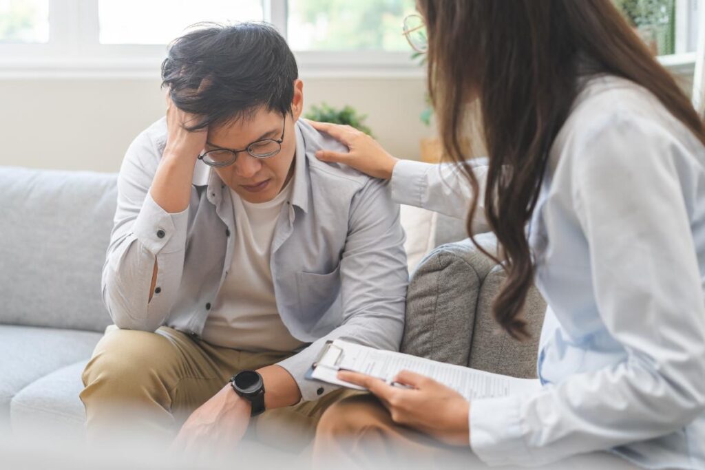 an upset man holds his hand to his temple while sitting at his therapy session asking his doctor what is coke bloat