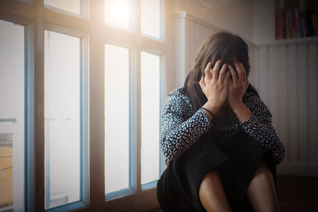 A woman sits with her knees to her chest and her head in her hands. She is struggling with cocaine addiction.