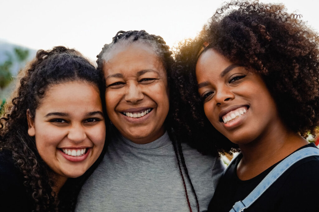 Three adult women of different generations are standing shoulder to shoulder and smiling.